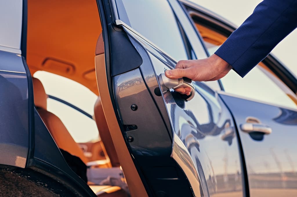 Close-up of a hand opening the rear door of a car with a tan leather interior